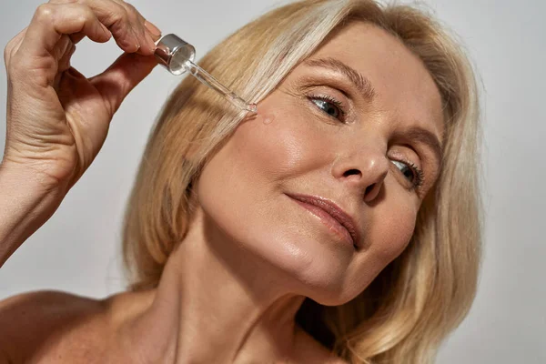 Mature woman dripping oil with dropper on her face — Stock Photo, Image