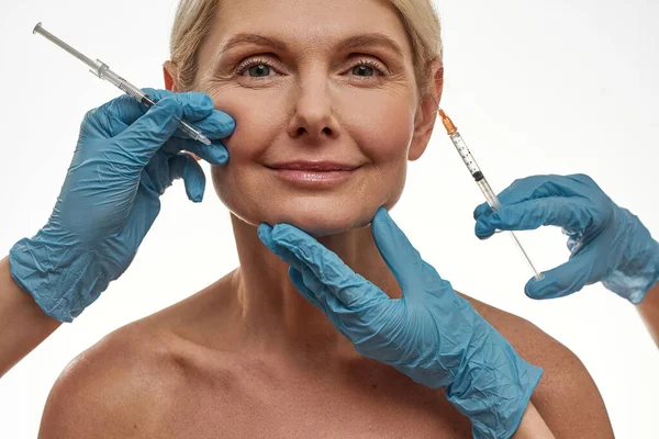 Lekarze wykonujący wstrzyknięcie na twarz dojrzałej kobiety — Zdjęcie stockowe