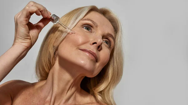 Mujer goteando aceite cosmético con gotero en la cara — Foto de Stock
