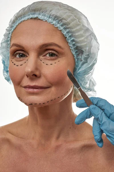 Mãos de cirurgião plástico com bisturi perto do rosto feminino — Fotografia de Stock