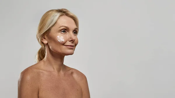 Mulher com creme cosmético no rosto olhando para longe — Fotografia de Stock