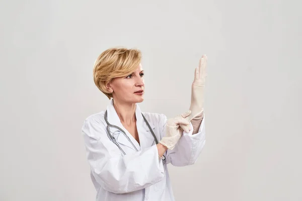 Olgun kadın doktor, lateks eldiveni takıyor. — Stok fotoğraf
