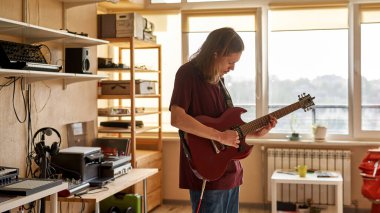 Odaklanmış adam evde elektro gitarla riff çalıyor.