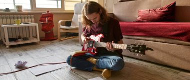 Konsantre adam yerde elektro gitarla oynuyor.