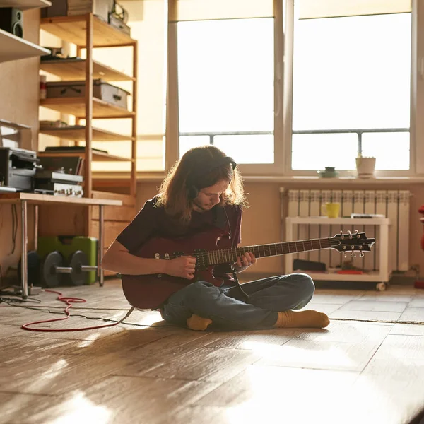 Uomo che suona la chitarra elettrica sul pavimento a casa soleggiata — Foto Stock