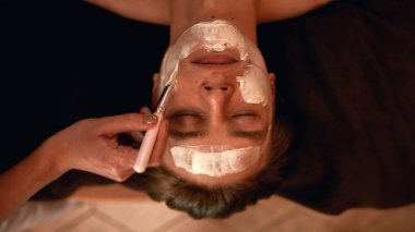 Güzellik uzmanı adamın yüzüne kozmetik krem sürüyor.