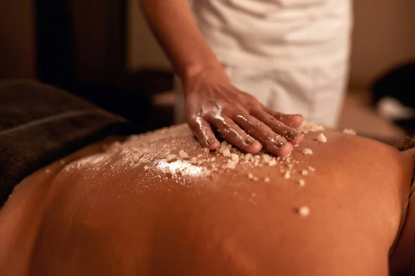 Masażysta zrobić peeling solny na dziewczynie z powrotem w salonie spa — Zdjęcie stockowe