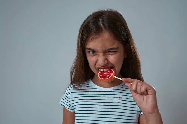 Little girl with face expression biting lollipop — Stock Photo, Image