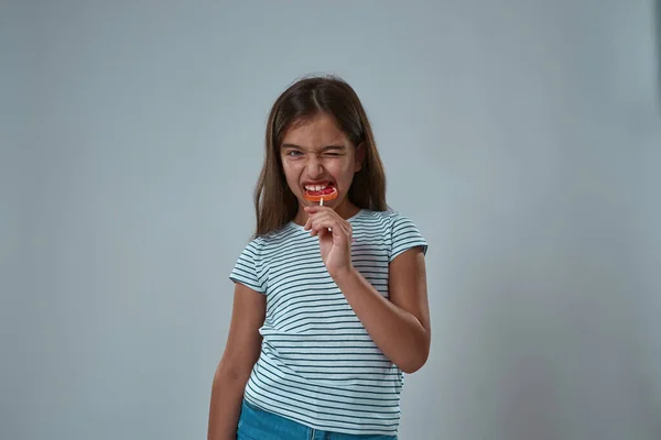 Front view of little girl biting sweet lollipop — Stock Photo, Image