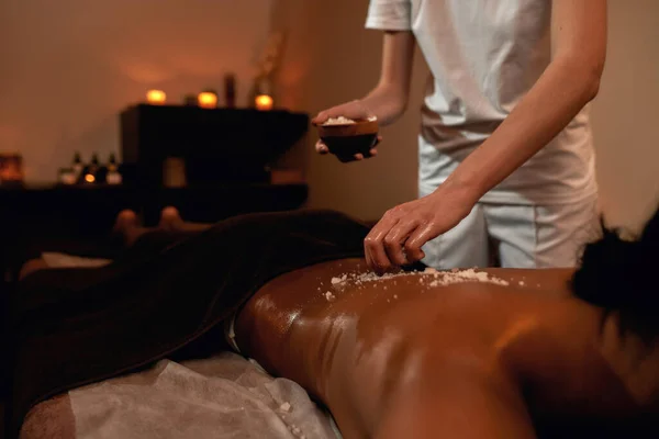 Masajista vertiendo sal sobre la mujer durante el exfoliante —  Fotos de Stock