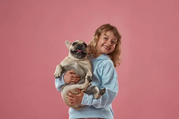 Приємна маленька дівчинка тримає і обіймає французьку бульдогу — стокове фото