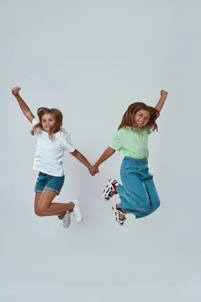 Zufriedene kleine Freundinnen halten Händchen und springen — Stockfoto