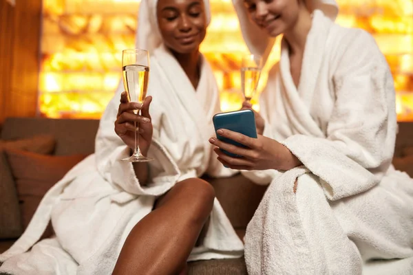 As mulheres usam telefone celular e bebem champanhe no spa — Fotografia de Stock