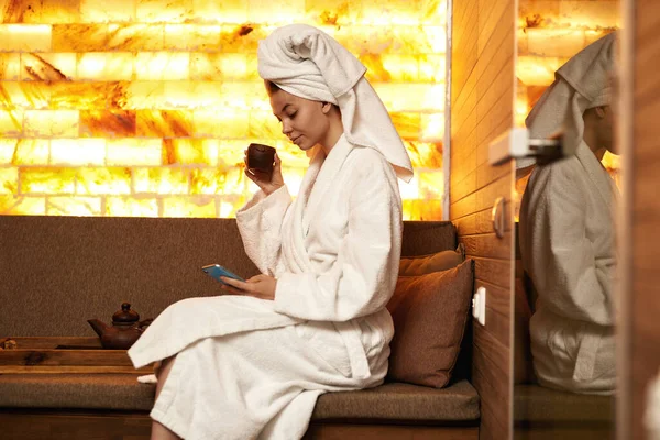 Meisje gebruik smartphone en drink thee in spa salon — Stockfoto