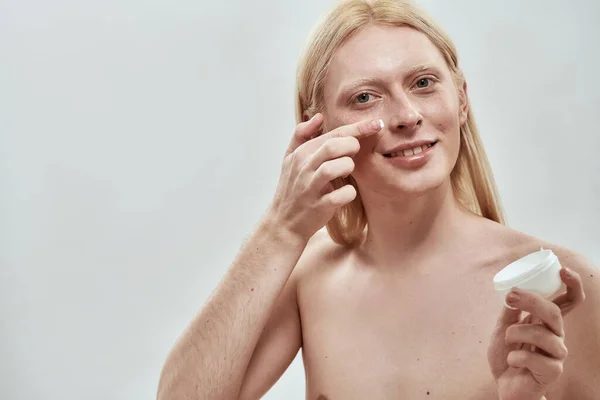 Guy smeert cosmetische crème uit container op gezicht — Stockfoto