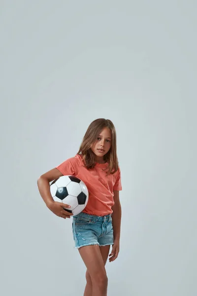 Серьёзная девочка, стоящая с футбольным мячом — стоковое фото