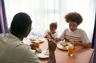 Baba ve oğul yemek yerken kız meyve suyu içiyor.