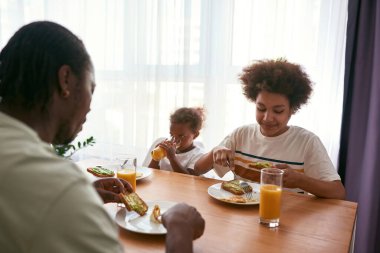 Baba ve oğul yemek yerken kız meyve suyu içiyor.