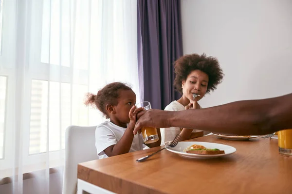 Çocuk babasının yanında yumurta yiyor. Kızının meyve suyu içmesine yardım ediyor. — Stok fotoğraf