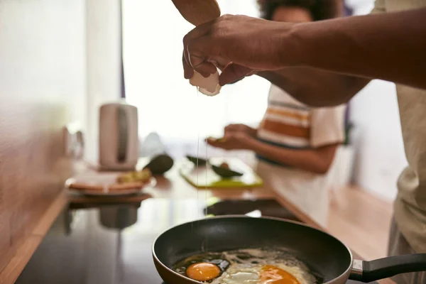 Pai quebrando ovo na panela perto filho fazendo sanduíche — Fotografia de Stock