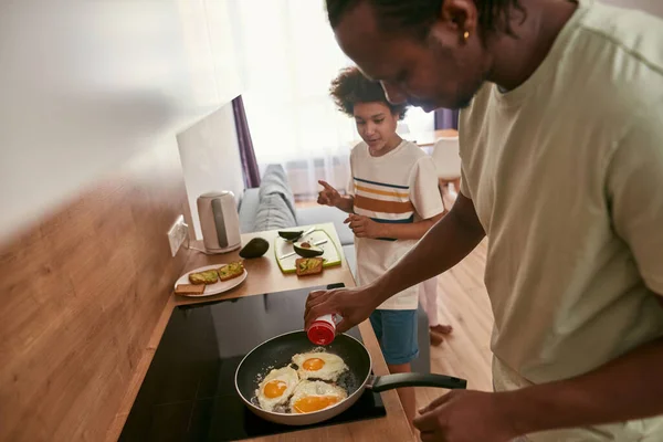 African father and son cooking breakfast at home