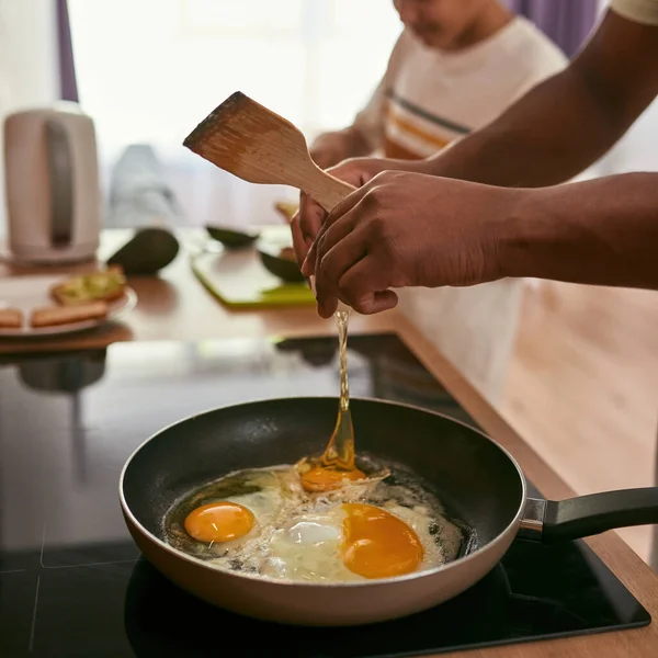 Человек разбивает яйцо на сковороде и сын готовит с киви — стоковое фото
