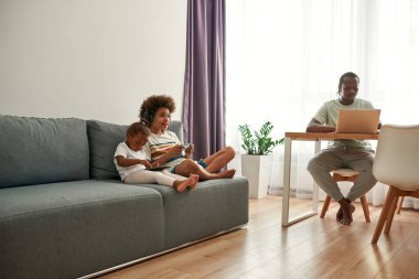 Çocuklar kanepede dinlenirken, babalar dizüstü bilgisayarda çalışıyor.