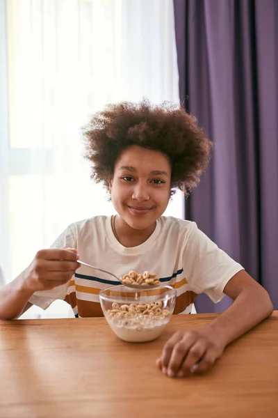 Niño sonriente comiendo cereales en la mesa de madera en casa — Foto de Stock