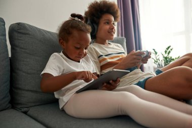 Siyah kardeş ve kızı evdeki kanepede dinleniyor.