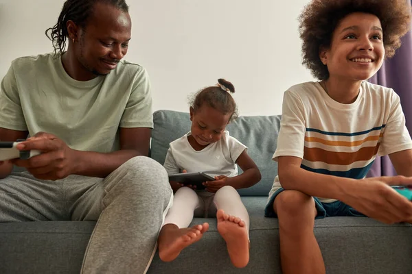 Μαύρη οικογένεια αναπαύεται με ψηφιακές συσκευές στο σπίτι — Φωτογραφία Αρχείου