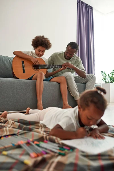 Ο πατέρας διδάσκει τον γιο να παίζει κιθάρα ενώ το κορίτσι ζωγραφίζει. — Φωτογραφία Αρχείου
