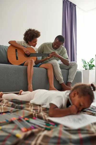 Πατέρας και γιος παίζουν κιθάρα κοντά στην κόρη ζωγραφίζουν. — Φωτογραφία Αρχείου