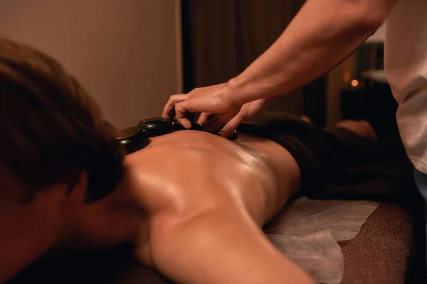 Parcial de massagistas colocando pedras quentes no homem de volta — Fotografia de Stock