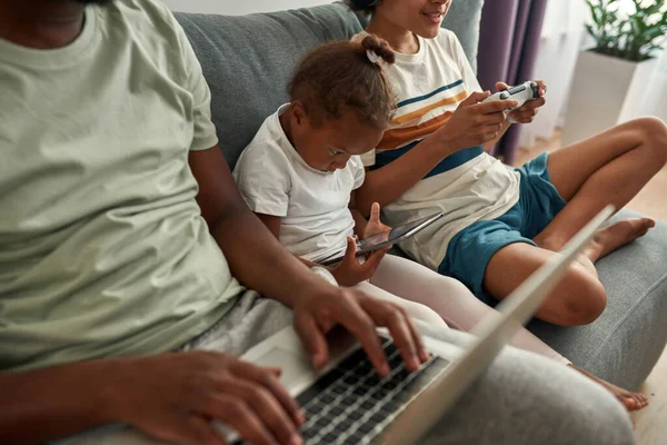 Istirahat keluarga kulit hitam dan menggunakan garget di sofa di rumah — Stok Foto