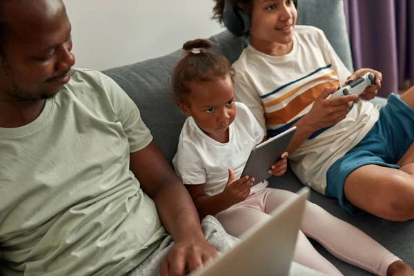 Μαύρος πατέρας και τα παιδιά χρησιμοποιούν gargets στον καναπέ στο σπίτι — Φωτογραφία Αρχείου