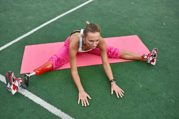 Disabled athletic girl stretching on sports field