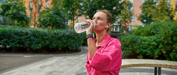 Chica deportiva bebiendo agua en el banco en la plaza de la ciudad —  Fotos de Stock