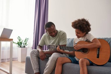 Erkek öğretmen ve oğlu akustik gitarla oynuyor.