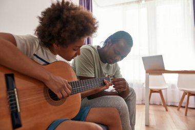 Siyah baba oğluna akustik gitar çalmayı öğretiyor.