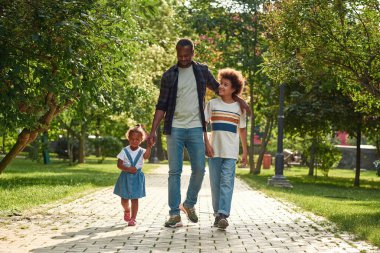 Çocuklu babam parkta kaldırımda yürüyor.