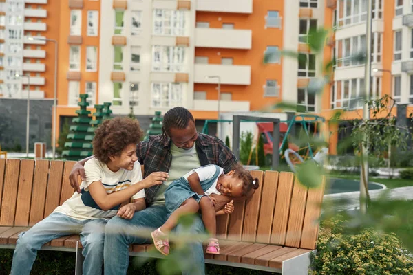 Šťastná černá rodina sedí a odpočívá na lavičce na dvoře — Stock fotografie