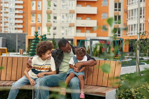 Černá rodina sedět a odpočívat na lavičce ve městě dvoře — Stock fotografie