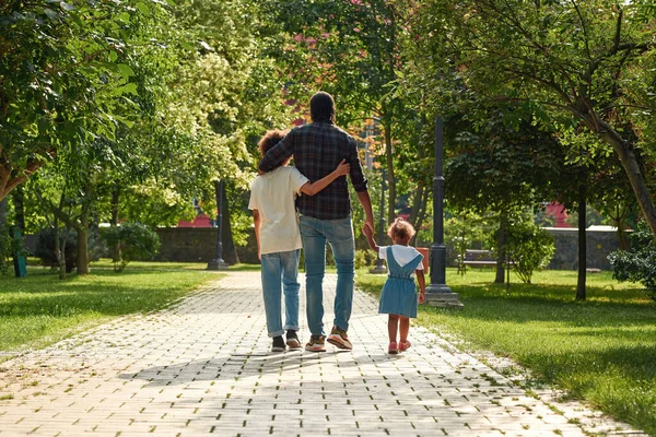 Svart familjevandring på asfalterad väg i solig park — Stockfoto