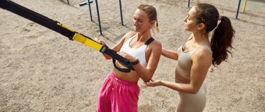 Kadın arkadaşının spor sahasında egzersiz yapmasına yardım ediyor.