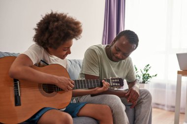 Baba gitar çalan genç çocuğa bakıyor.