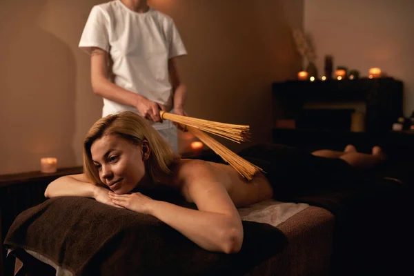 Masseur faz massagem de menina de resto com paus em spa — Fotografia de Stock