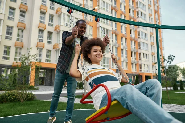 Černošky otec houpání usmívající se dospívající syn na houpačce — Stock fotografie