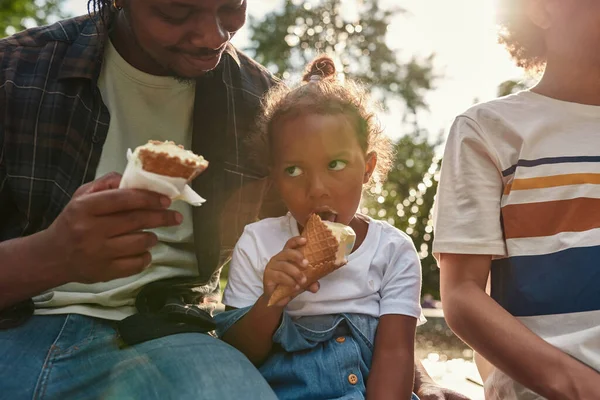 Baba, kız ve oğul parkta dondurma yiyorlar.