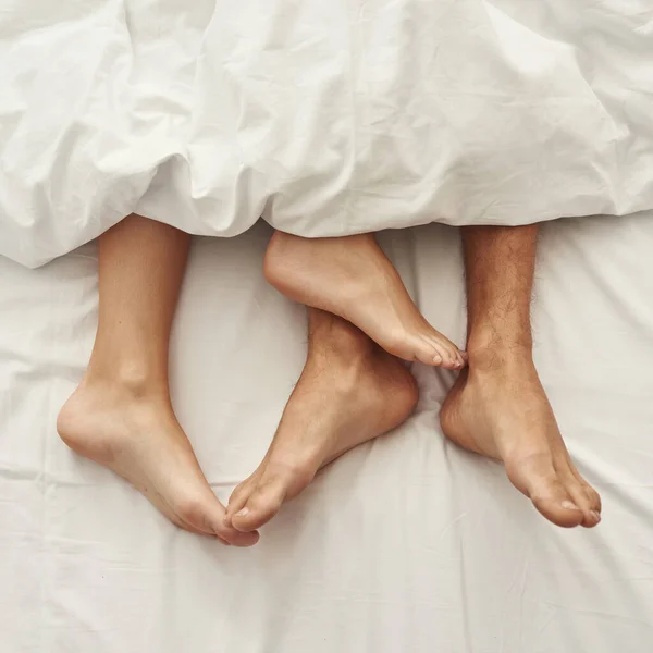 Partial of barefoot feet of man and woman on bed
