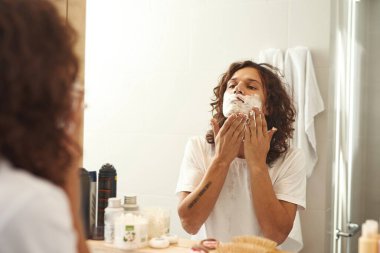 Banyoda yüzüne köpük süren genç bir adam.